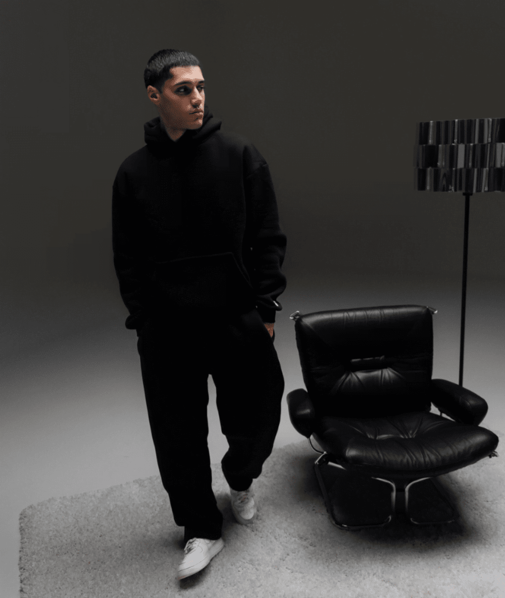 Junger Mann gekleidet in schwarzen Hoodie und Jogger sowie weißen Sneakers